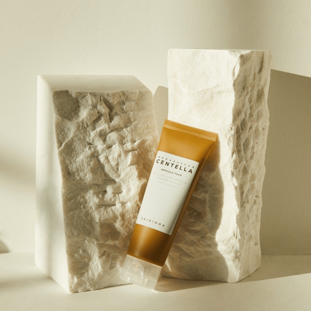 SKIN1004 Madagascar Centella Ampoule Foam standing against light stone blocks in natural sunlight, with its brown and white tube design and elegant minimalism.