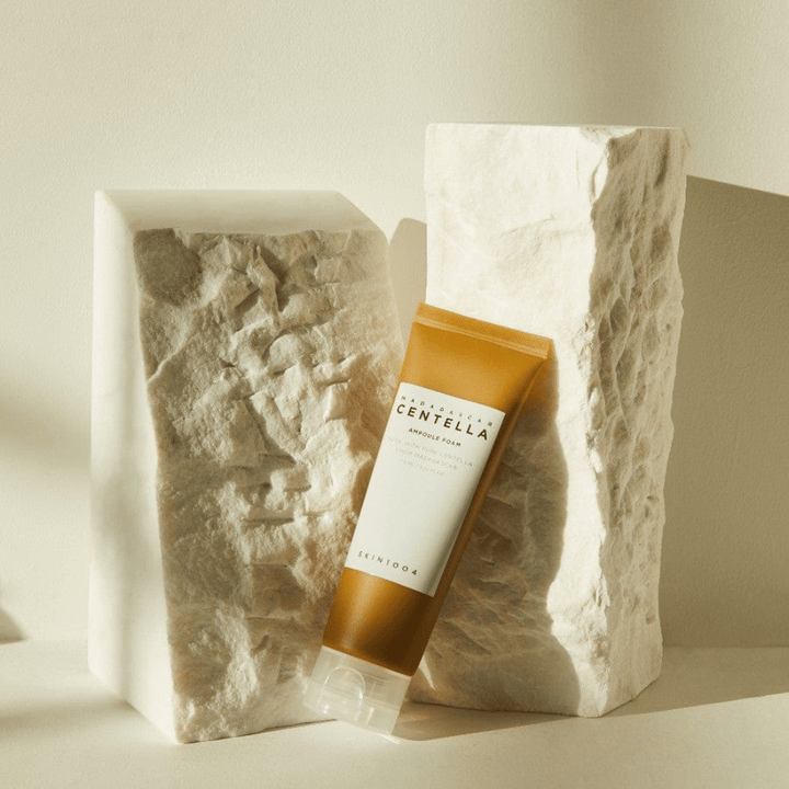 SKIN1004 Madagascar Centella Ampoule Foam stående mot ljusa stenblock i naturligt solljus, med sin brunvita tubdesign och elegant minimalism.