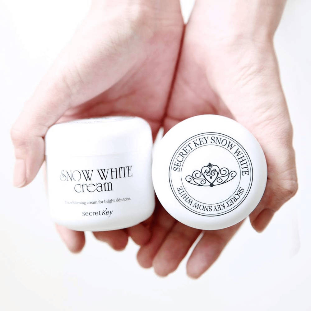 Two jars Secret Key Snow White Cream held in hands, one showing the lid and one showing the front.