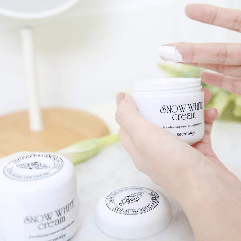 Hand picking up white cream from a jar Secret Key Snow White Cream on a makeup table.