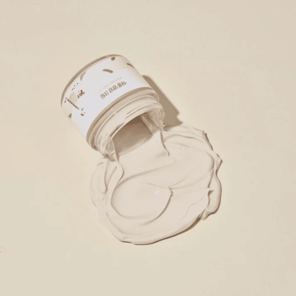 Mixsoon Soybean Nourishing Cream spilled from the jar on a beige background. The cream's rich texture shows its intense moisturizing properties.