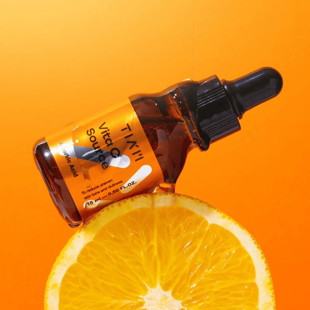TIA'M Vita C Source bottle placed against an orange and an orange background symbolizing the freshness and antioxidant effect of vitamin C.