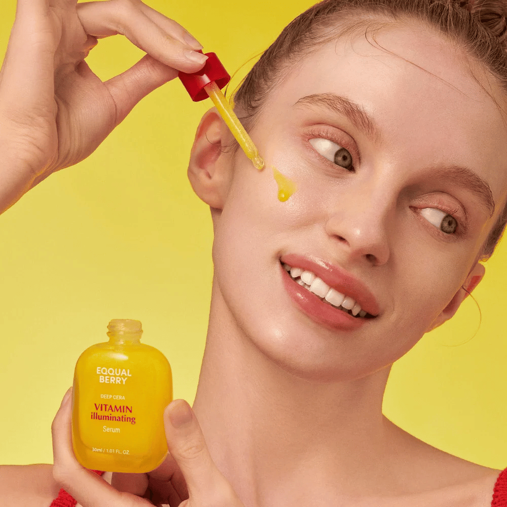 Smiling woman applies Equal Berry Vitamin Illuminating Serum with a pipette. Fresh and radiant skin against a lively yellow background that matches the serum's color.