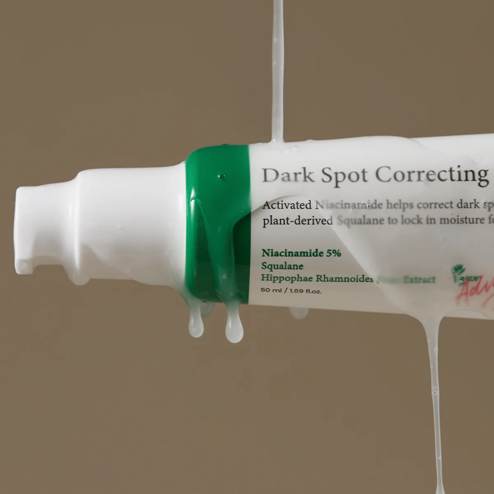 Close-up of a pump bottle of Axis-Y Dark Spot Correcting Glow Serum with white packaging and green cap, covered by running transparent liquid.