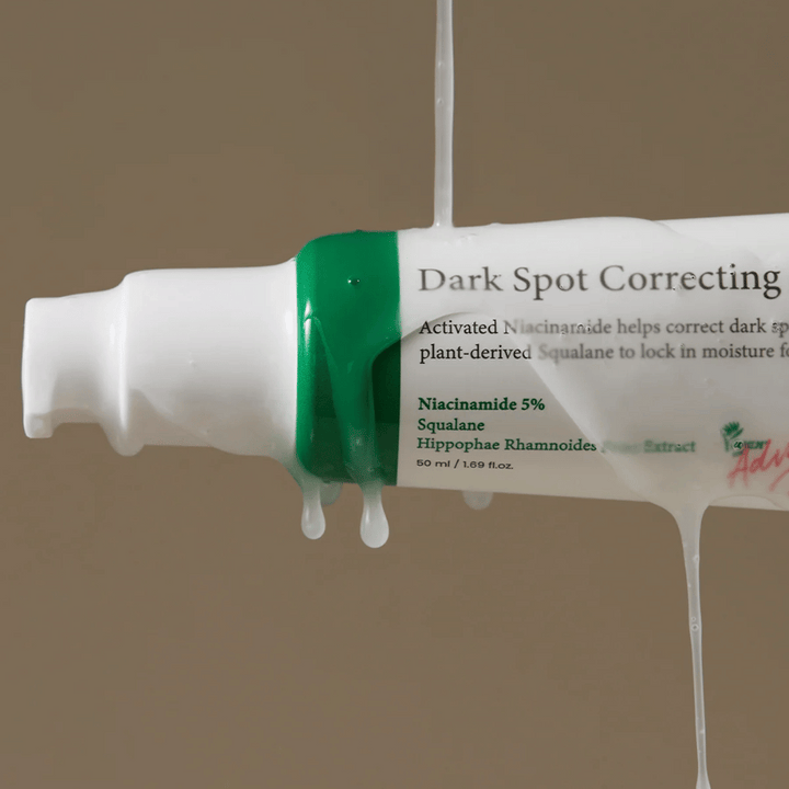 Närbild på en pumpflaska av Axis-Y Dark Spot Correcting Glow Serum med vit förpackning och grön kork, täckt av rinnande genomskinlig vätska.