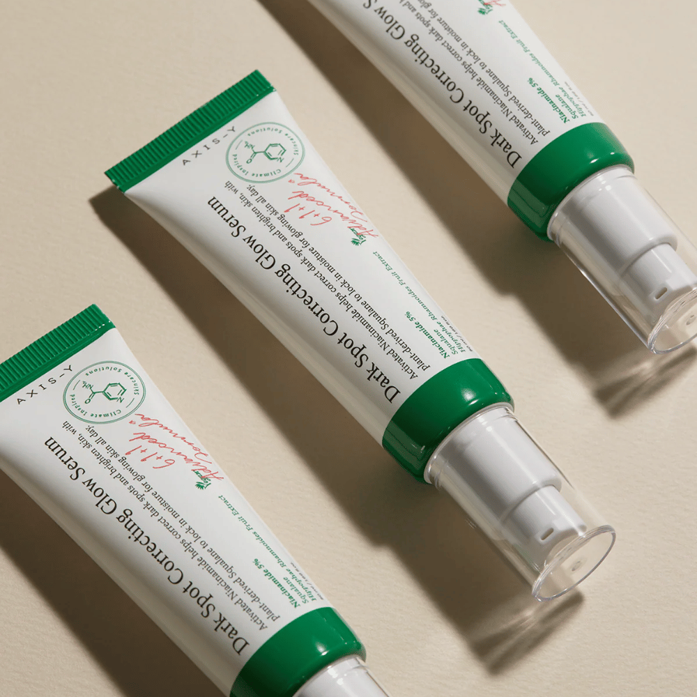 Three tubes of Axis-Y Dark Spot Correcting Glow Serum with green cap and white packaging are lying on a light surface.