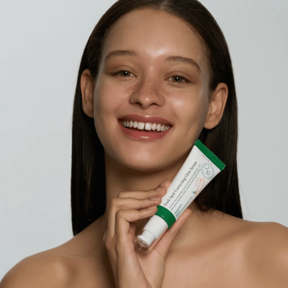 A young woman is holding a tube of AXIS - Y Dark Spot Correcting Glow Serum 50ml.