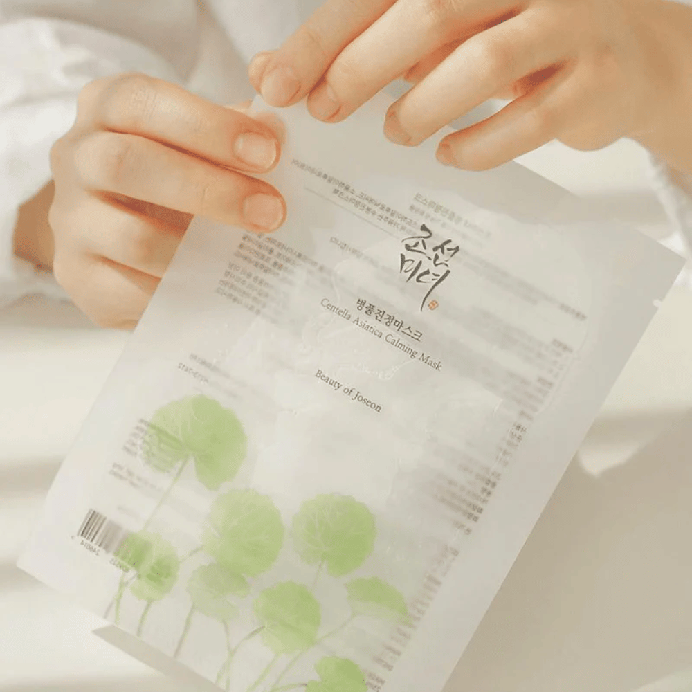 A person holding up a sheet of paper with a Beauty of Joseon Centella Asiatica Calming Mask 1 pc on.