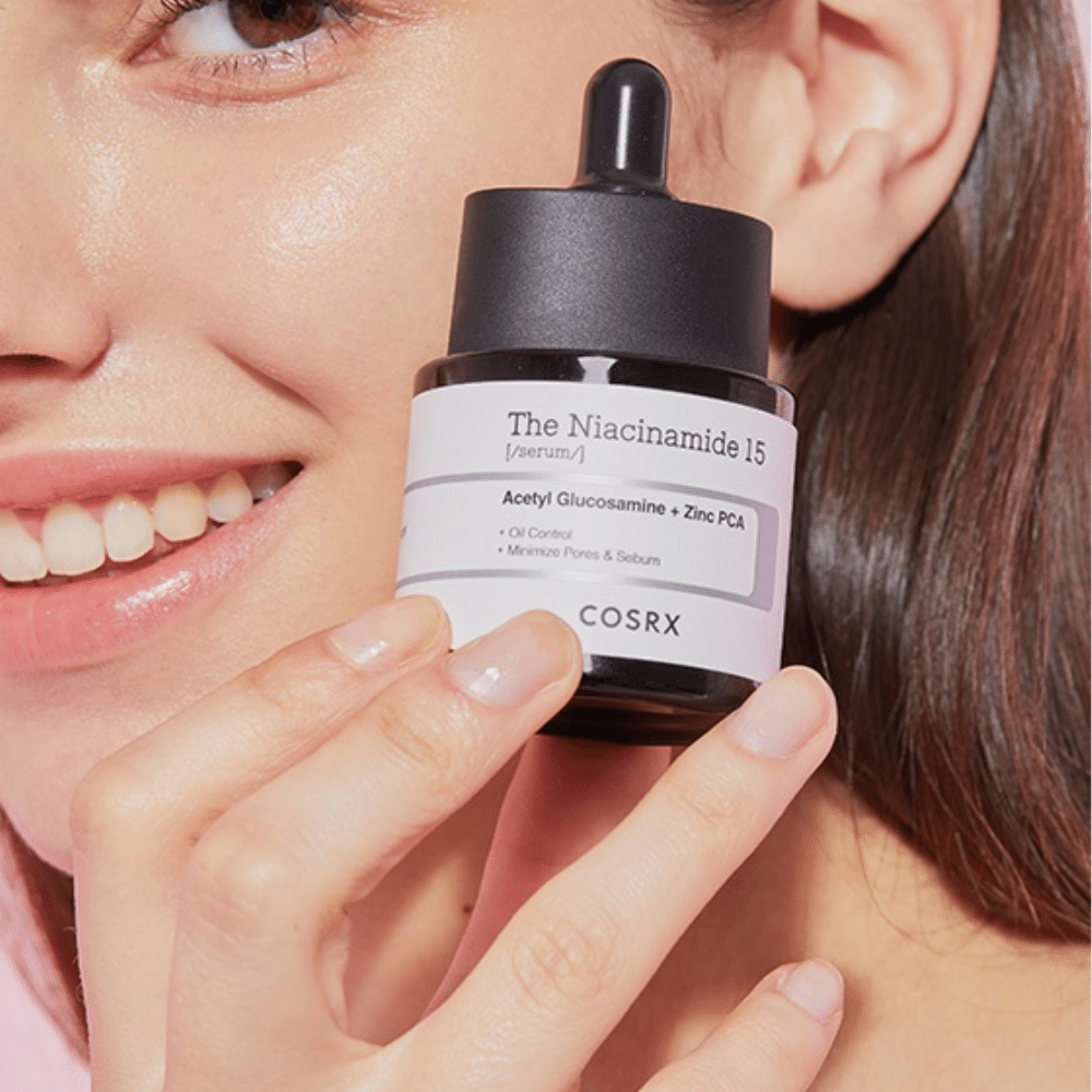 A woman is holding a bottle of COSRX Niacinamide 15 Serum 20ml for niacinamide and sebum production.