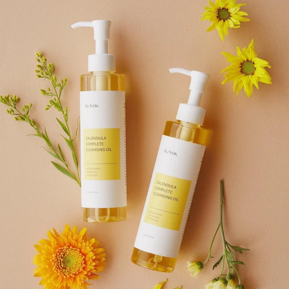 Two bottles iUNIK Calendula Complete Cleansing Oil 200ml with yellow flowers on a beige background, infused with plant oil.