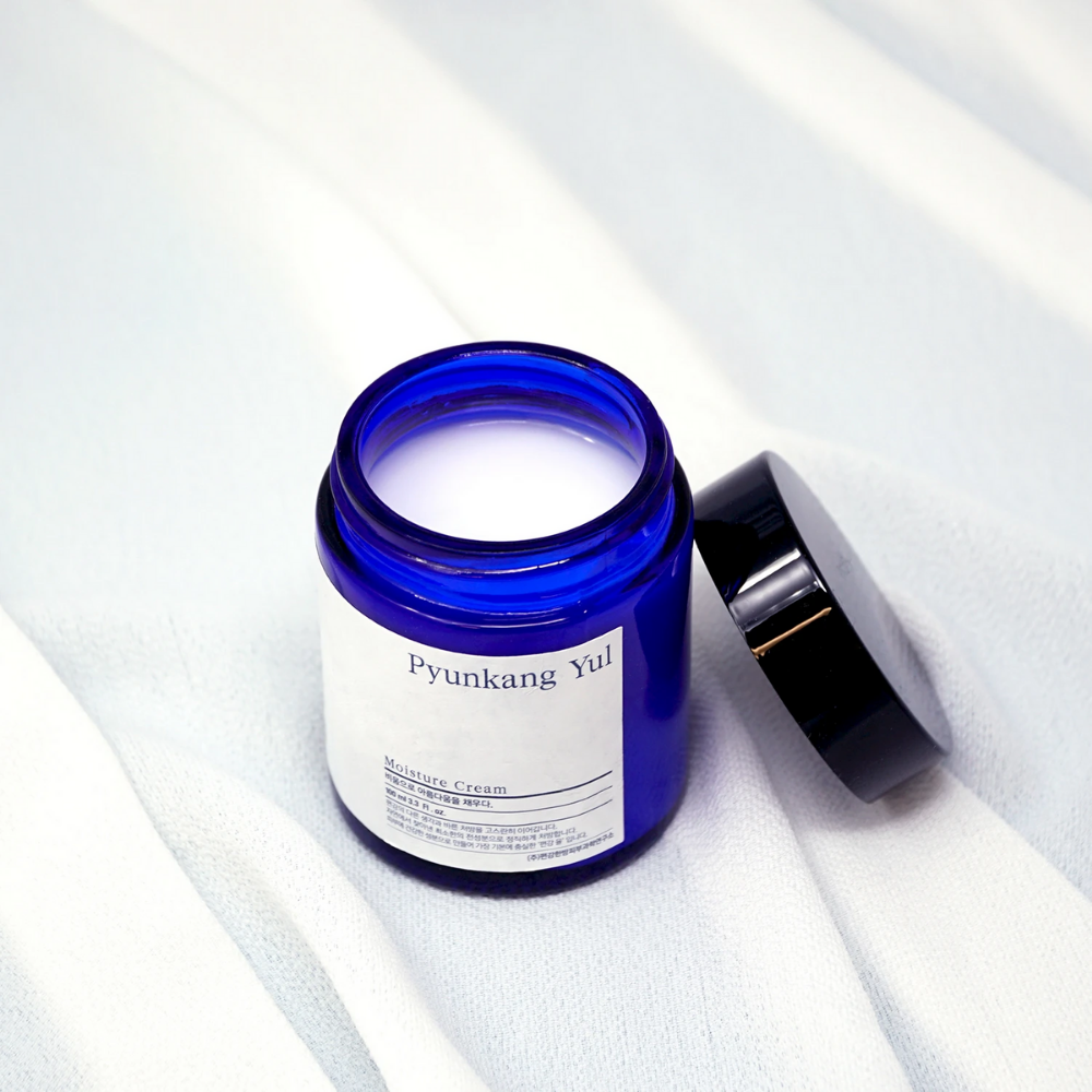 A blue jar with a lid sitting on top of a white cloth showcasing Pyunkang Yul's Moisture Cream 100ml moisturizing properties.